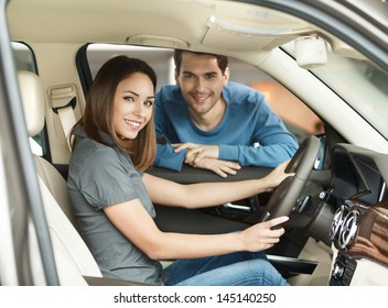 Proud Of Their New Car. Beautiful Young Couple Are Examining A New Car At The Dealership