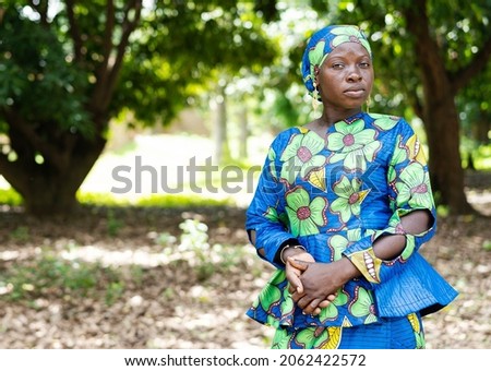 Proud young African woman in an elegant blue and green dress and matching headgear looking grimly at the camera
