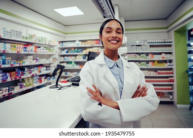 Proud young female with folded hands in labcoat standing in chemist near counter - Powered by Shutterstock