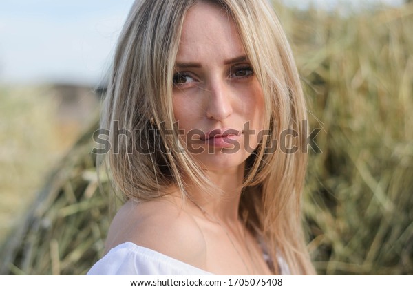 provincial young woman of blonde, of Eastern\
European descent in a white dress posing against a background of\
haystacks. A young girl from the village, a haystack, a farmer\
girl, national\
economy.