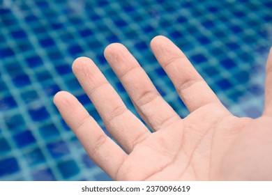 Pruney and wrinkled skin hand and finger from water on blue pool swimming background at morning sunrise,Skin symptoms of hands and fingerprints,Healthy looking hands,Skin treatment. - Shutterstock ID 2370096619