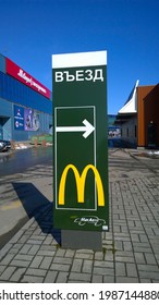 Pskov, Russia - March, 2021: Green Banner Of McDonald's Fast Food Cafe With Exit Sign And Directional Arrow For Car Buyers. City Street. McCafe Logo. Delivery Service. American Hamburger. Signpost.