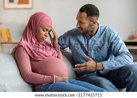 Psychological Abuse. Aggressive black man arguing with upset pregnant muslim wife at home, islamic couple awaiting baby quarreling while sitting on couch in living room, husband screaming at spouse