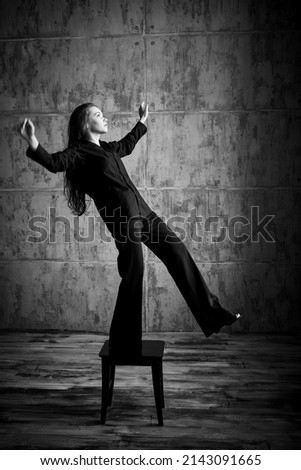 Psychological art portrait. A girl in a black shirt and trousers stands on a stool in a dark room and takes a step forward. The human inner world, psychological problems. Black and white portrait.