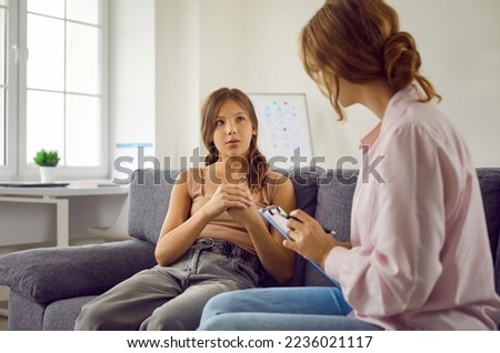 Psychologist listening to child. Professional therapist working with teenage child. Adolescent girl sitting on sofa and answering questions that school psychologist asks her. Therapy concept