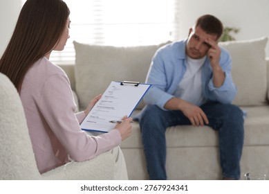 Psychologist making notes during therapy session with client indoors, selective focus