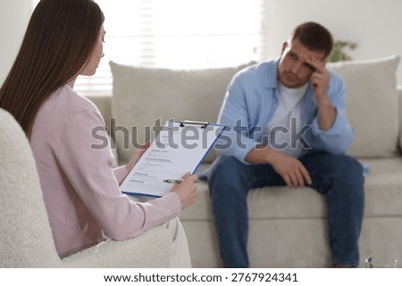 Psychologist making notes during therapy session with client indoors, selective focus
