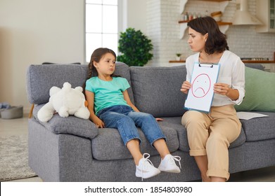 Psychologist With Picture Of Unhappy Emoticon Having Therapy Session With 8 - 10 Year Old Girl And Teaching Her Emotion Management. Private Therapist And Sad Child Solving Emotional Problems At Home