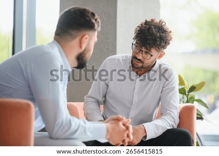 Psychologist taking notes while listening to male patient talking about problems during therapy session