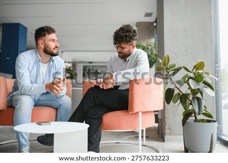 Psychologist taking notes while listening to male patient talking about problems during therapy session in modern office