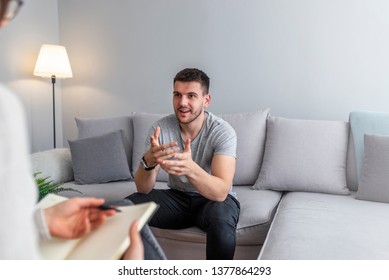 Psychologist talking with happy man in the office. Image of young man during psychological therapy. Female psychologist consulting man during psychological therapy session