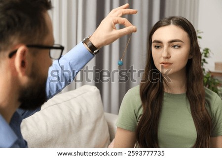 Psychologist using pendulum while working with patient during hypnosis session indoors, closeup
