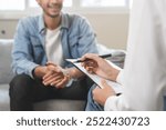 Psychology, depression. Happy smile asian young man patient mental therapy explain symptom with psychologist while doctor woman taking notes at clinic. Psychologist with sick mental health person.