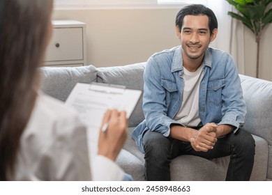 Psychology, depression. Happy smile asian young man patient mental therapy explain symptom with psychologist while doctor woman taking notes at clinic. Psychologist with sick mental health person. - Powered by Shutterstock