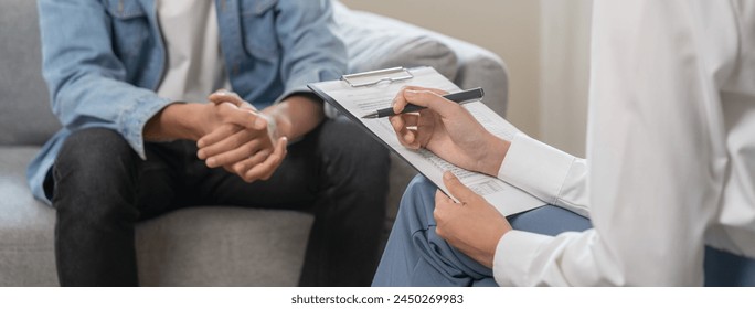 Psychology, depression. Suffer asian young man consultation with psychologist while patient counseling mental therapy, doctor hand taking notes at clinic. Psychologist with sick mental health person. - Powered by Shutterstock