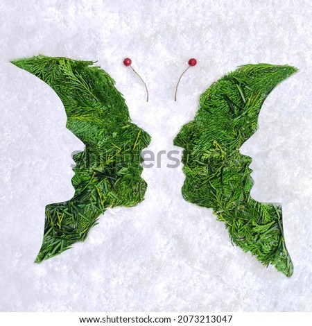 Psychology and optical illusion abstract concept four faces butterfly image. Flat lay arrangement of different shapes and color of arborvitae leaves against snowy white background.