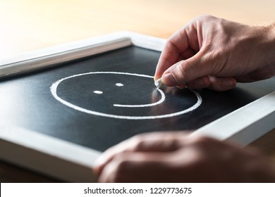 Psychology, psychiatry and mental health concept. Fighting depression and anxiety. Stay positive. Good self confidence and esteem. Man drawing happy face on blackboard, chalkboard.