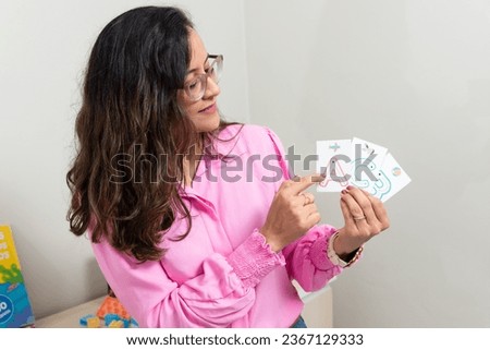 A psychopedagogue wearing pink clothes, wearing glasses, showing cards with letters of the alphabet. Educational help. Mental health care.