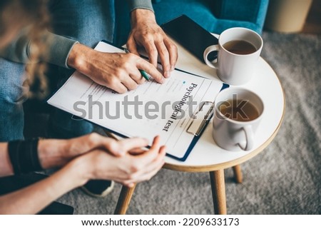 Psychotherapist with clipboard and pen consults fraught woman making closed gestures while sitting on comfortable couch in clinic office close view