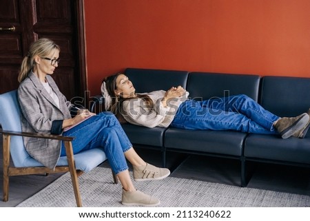 The psychotherapist listens attentively and writes down in a notebook what the patient is saying while lying on the couch.