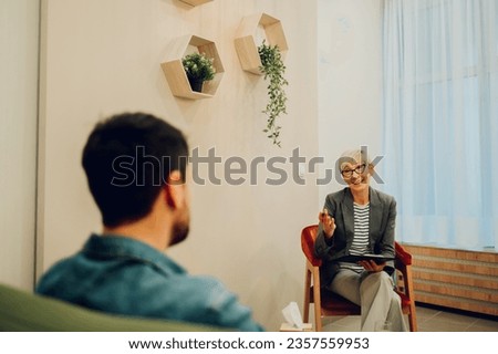 A psychotherapist is sitting with a client and having a session in the office. A female therapist is sitting with a patient in the office and giving him support and advice. Mental health awareness day