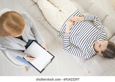 Psychotherapy concept, high angle view of therapist making notes while female patient is lying on the couch and talking - Powered by Shutterstock