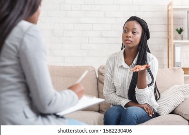 Psychotherapy concept. Sad afro lady sharing her problems at counselor's office, sitting on couch and emotionally telling something