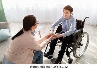 Psychotherapy consultation. Counselor offering help and support to disabled teen boy in wheelchair at office. Friendly female psychologist having session with handicapped youth, holding his hands
