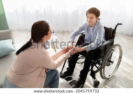 Psychotherapy consultation. Counselor offering help and support to disabled teen boy in wheelchair at office. Friendly female psychologist having session with handicapped youth, holding his hands