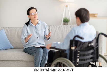 Psychotherapy for disabled teens. Young female psychologist speaking with teenage boy in wheelchair at office. Handicapped youth having session with counselor indoors