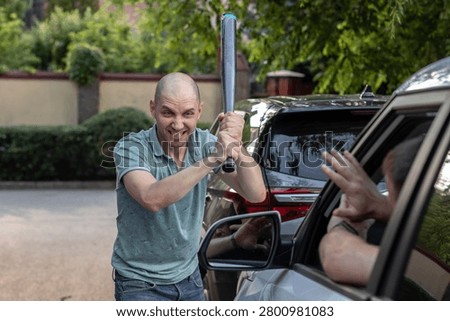A psychotic, aggressive man attacking another man's car with a baseball bat.