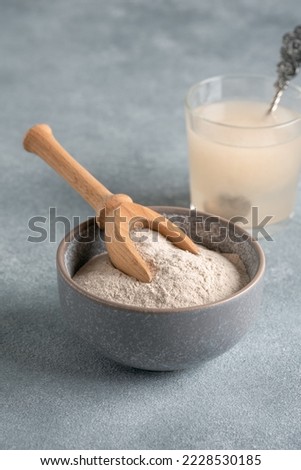 Psyllium husk powder in bowl and glass with of water soluble fiber for intestinal, gray background. Gluten free diet concept. Side view, selective focus, vertical