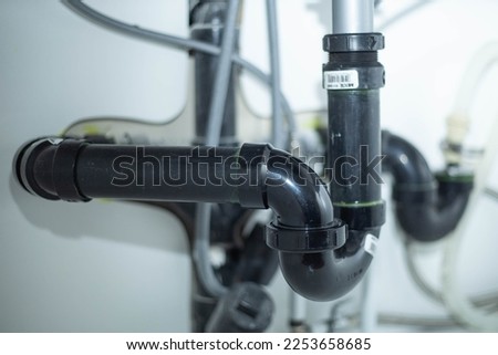 P-trap pvc plumbing under a kitchen sink with various hoses in the background
