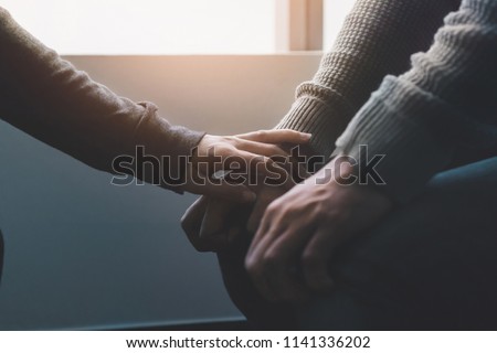 PTSD Mental health concept, Psychologist sitting and touch hand young depressed asian man for encouragement near window with low light environment.Selective focus.