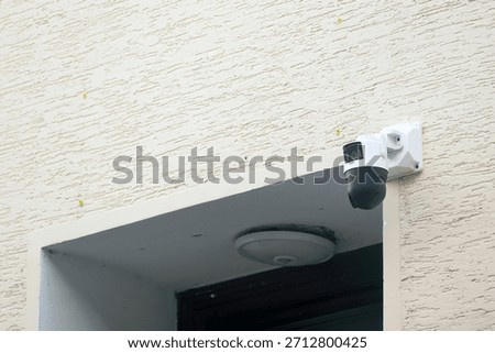 PTZ security camera installed on building wall above an entrance. Represents pan-tilt-zoom surveillance, smart house monitoring, contemporary security technology, and digital safety infrastructure.