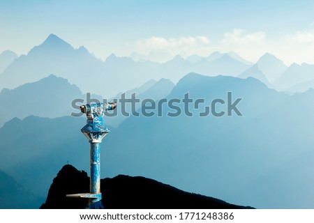 Public binoculars provide far view to distant blue mountain ranges silhouette in early Morning Sunlight. Foresight and vision for new and creative business concept and ideas. Alps, Allgau Bavaria Ge