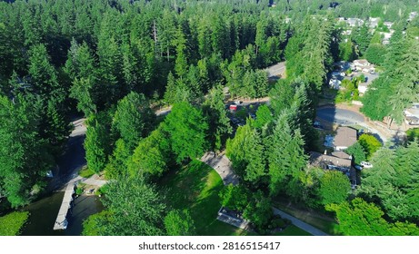 Public boat launch facilities include wooden pier, paved access roads, dense pine trees in Seattle suburbs. Shaded paths, park grounds connect to tranquil waters in Kent, King County, WA. USA