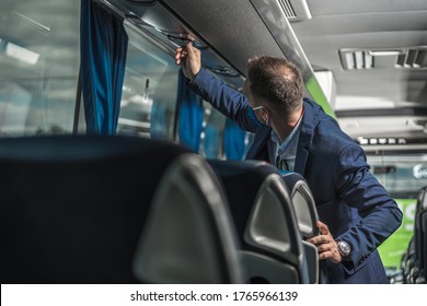 Public Coach Bus Driver With Protective Face Mask On Checking Air Fan Above Passenger Seats. 