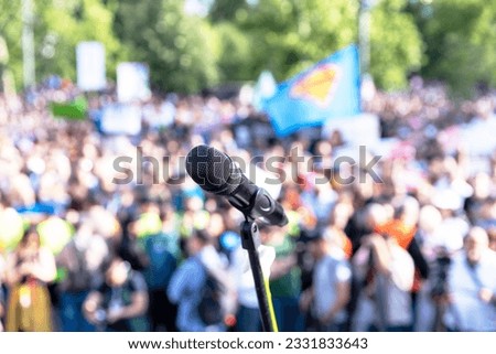 Public communication concept. Microphone in focus at mass protest or public demonstration, blurred crowd of people in the background