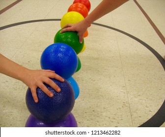 In a public, crowded, fun gymnasium, under fluorescent lights, are colorful dodge balls, perched upon a matching cone, ready for a child to grab and throw them into action from the mid-court circle - Shutterstock ID 1213462282