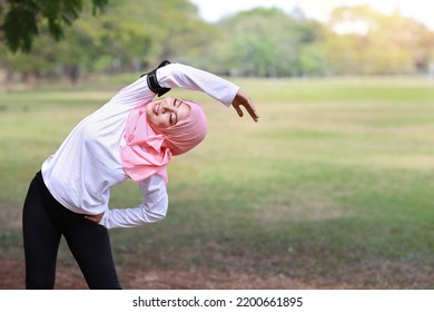 Public Exercise Lifestyle Concept, Fitness Woman Listening Music From Wireless Earphones And Mobile Phone. Rear View Athletic Young Asian Girl In Muslim Sportswear Standing, Stretching After Workout 