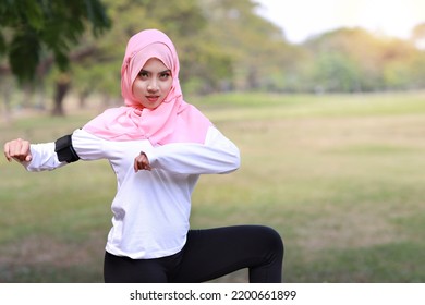 Public Exercise Lifestyle Concept, Fitness Woman Listening Music From Wireless Earphones And Mobile Phone. Rear View Athletic Young Asian Girl In Muslim Sportswear Standing, Stretching After Workout 