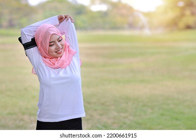 Public Exercise Lifestyle Concept, Fitness Woman Listening Music From Wireless Earphones And Mobile Phone. Rear View Athletic Young Asian Girl In Muslim Sportswear Standing, Stretching After Workout 