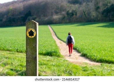 Public footpath sign in the countryside with a hiker on the path.