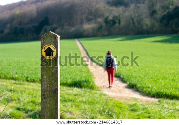Public footpath sign in the countryside with a\
hiker on the path.