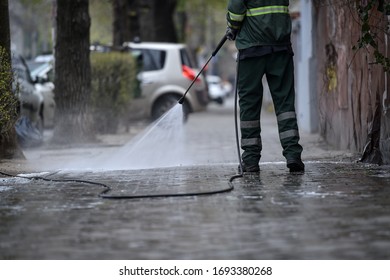 Public janitor deep cleaning the sidewalk with high pressure disinfectant solution in times of corona virus pandemic in a lockdown Bucharest, Romania