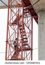 Public Mass Transportation Project Is Under Construction. Worker Is Walking On Red Ladder To The Top Of High Concrete Pillar.