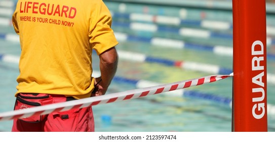 A Public Pool Life Guard Or Pool Safety Officer In Uniform Standing Duty Or Guard Supervising Swimming And Children Preventing Drowning Accidents. 