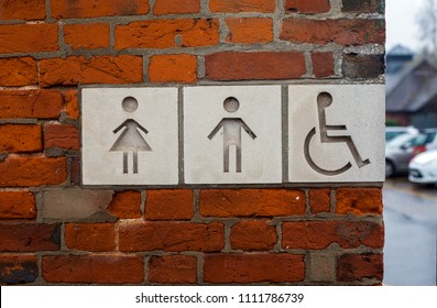 Public toilet street sign with male, female and disabled people icons on it. The sign is made of white stone mounted in the brick wall