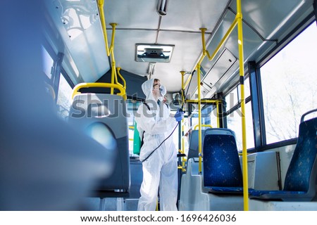 Public transportation healthcare. Man in white protection suit disinfecting and sanitizing handlebars and bus interior to stop spreading highly contagious coronavirus or COVID-19.